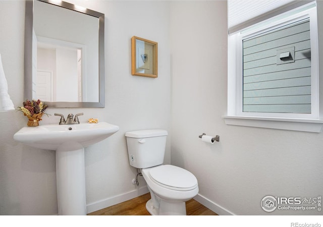 half bath with toilet, baseboards, and wood finished floors