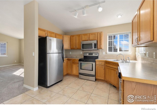 kitchen featuring light colored carpet, lofted ceiling, light tile patterned floors, appliances with stainless steel finishes, and a sink