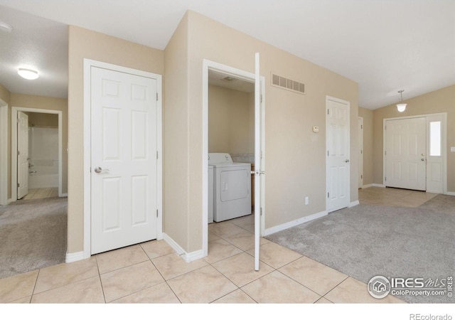 foyer entrance featuring light tile patterned floors, visible vents, washer / clothes dryer, and light colored carpet