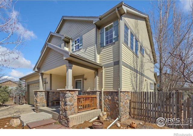 view of front of property with a garage, stone siding, a porch, and fence