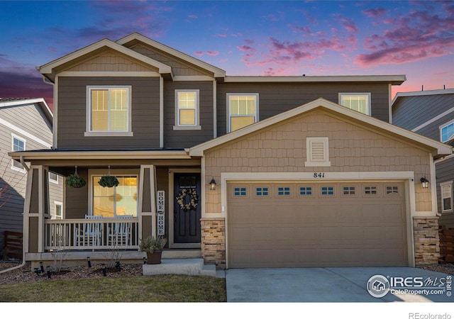 view of front of home featuring stone siding, driveway, a porch, and an attached garage