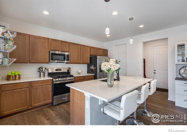 kitchen featuring a kitchen bar, decorative light fixtures, appliances with stainless steel finishes, brown cabinetry, and dark wood-style flooring