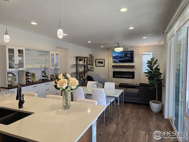 kitchen with a textured ceiling, dark wood finished floors, white cabinetry, a stone fireplace, and glass insert cabinets