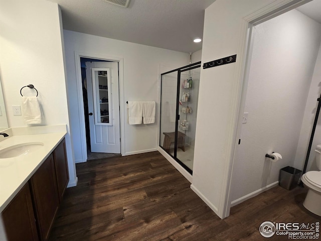 bathroom with a stall shower, toilet, vanity, and wood finished floors