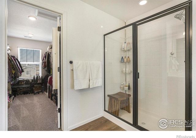 full bathroom featuring wood finished floors, visible vents, baseboards, a stall shower, and a walk in closet