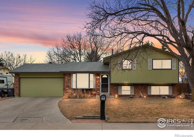 tri-level home with a front yard, a garage, brick siding, and driveway