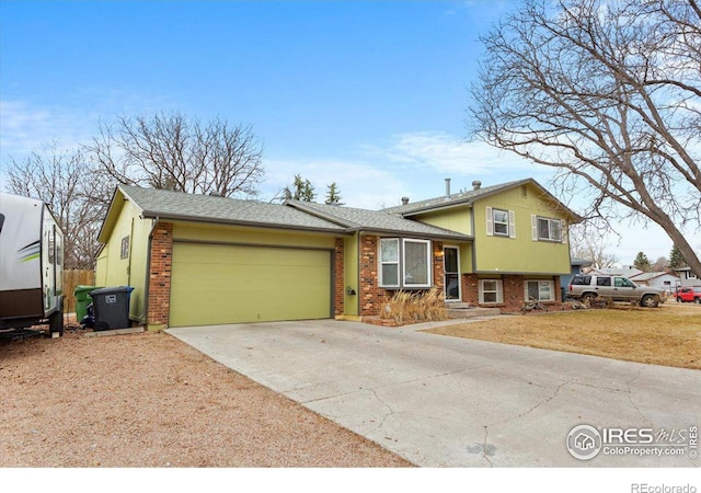 tri-level home with a front lawn, concrete driveway, a shingled roof, a garage, and brick siding