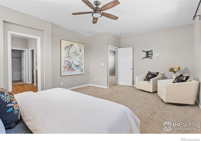 carpeted bedroom with visible vents, a ceiling fan, a walk in closet, and baseboards