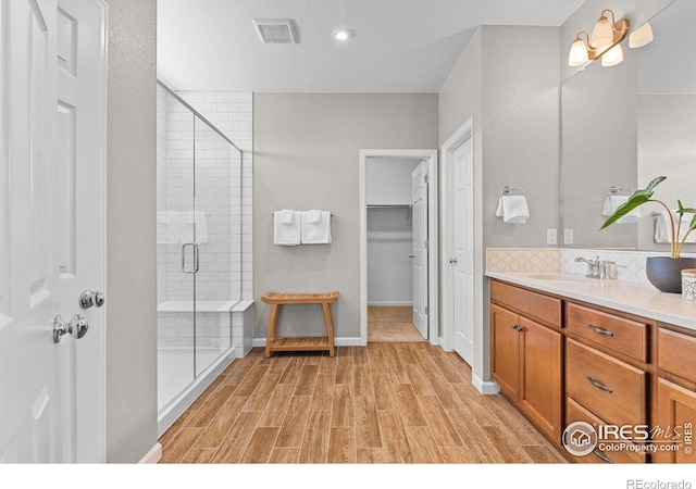 full bath featuring visible vents, a stall shower, wood finished floors, baseboards, and vanity