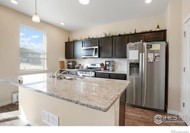 kitchen featuring visible vents, a sink, stainless steel appliances, light wood finished floors, and dark brown cabinets