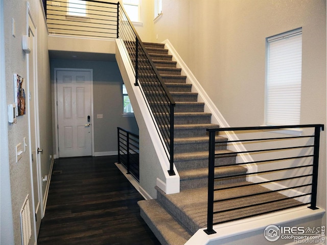 staircase with plenty of natural light, wood finished floors, visible vents, and baseboards