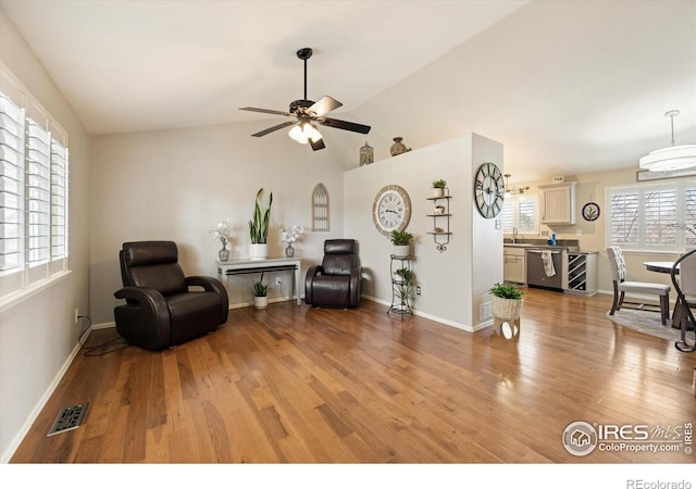 living area featuring baseboards, visible vents, ceiling fan, vaulted ceiling, and light wood-type flooring