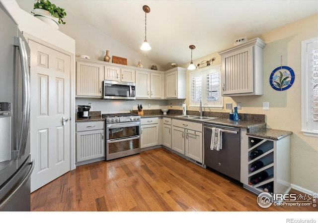 kitchen featuring pendant lighting, vaulted ceiling, wood finished floors, stainless steel appliances, and a sink