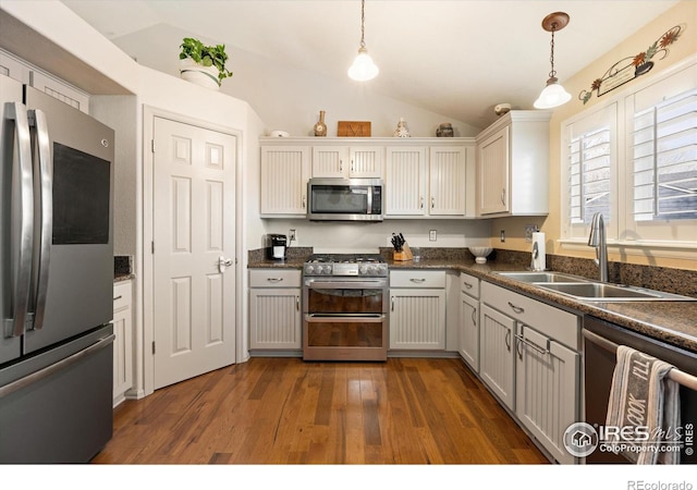 kitchen featuring dark wood-type flooring, a sink, dark countertops, stainless steel appliances, and hanging light fixtures