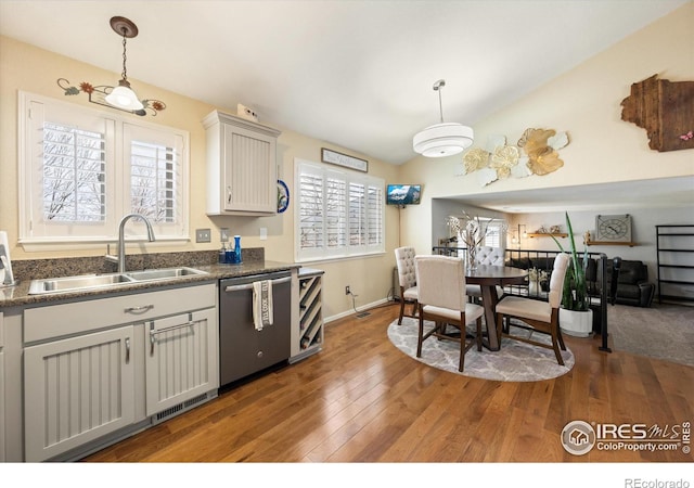 kitchen featuring a sink, decorative light fixtures, stainless steel dishwasher, dark countertops, and wood finished floors