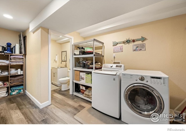 washroom featuring wood finished floors, baseboards, washing machine and clothes dryer, laundry area, and a sink