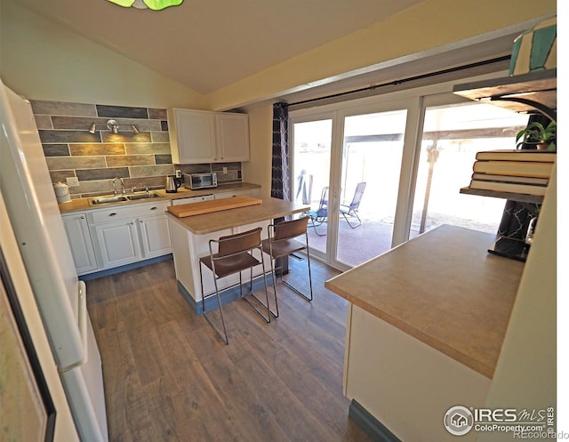 kitchen featuring dark wood-style floors, lofted ceiling, a sink, decorative backsplash, and white cabinets