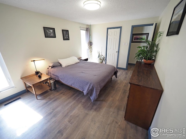 bedroom with dark wood finished floors, baseboards, visible vents, and a textured ceiling