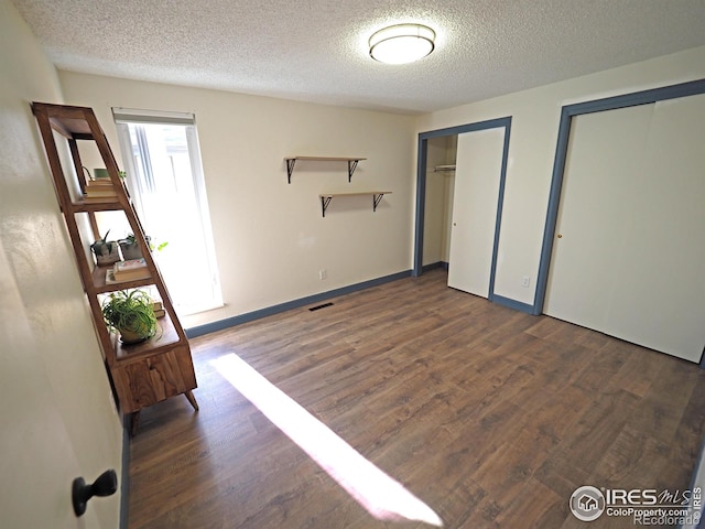 unfurnished bedroom featuring visible vents, two closets, a textured ceiling, wood finished floors, and baseboards