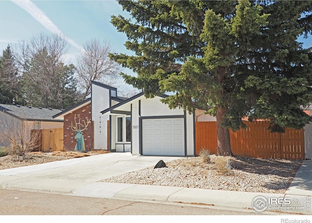 view of front of house with concrete driveway, an attached garage, and fence