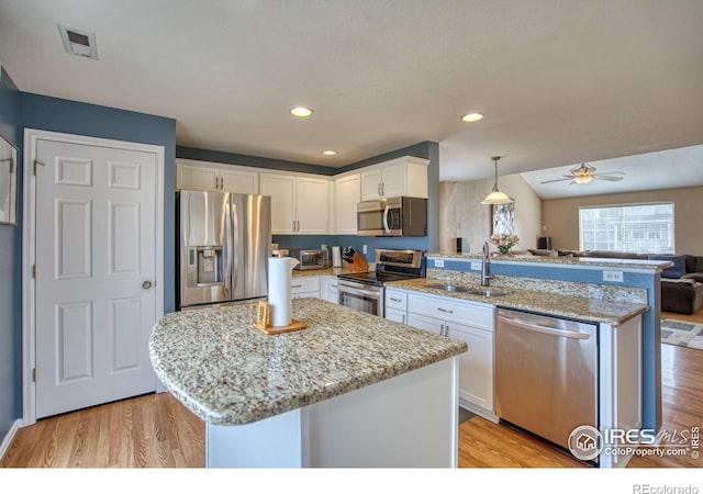 kitchen featuring open floor plan, a peninsula, stainless steel appliances, white cabinetry, and a sink