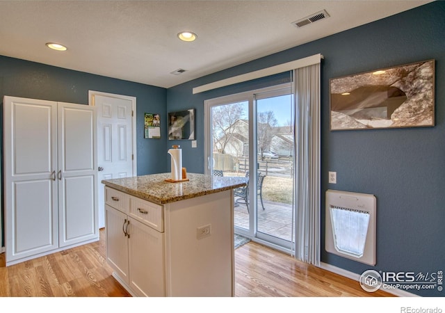 kitchen featuring white cabinets, light stone countertops, visible vents, and light wood finished floors