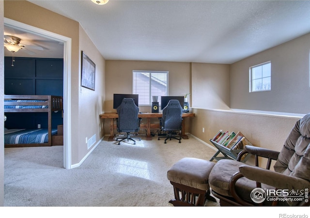 carpeted office space featuring visible vents, a textured ceiling, a ceiling fan, and baseboards