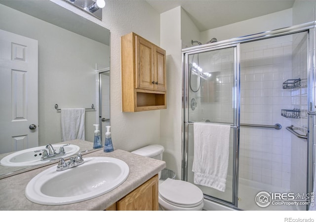 full bathroom featuring tiled shower, toilet, vanity, and a textured wall