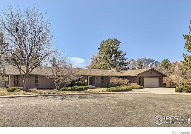 ranch-style home with a mountain view, an attached garage, a chimney, and driveway