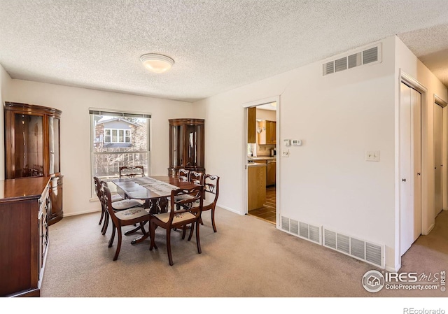 carpeted dining area featuring visible vents, baseboards, and a textured ceiling