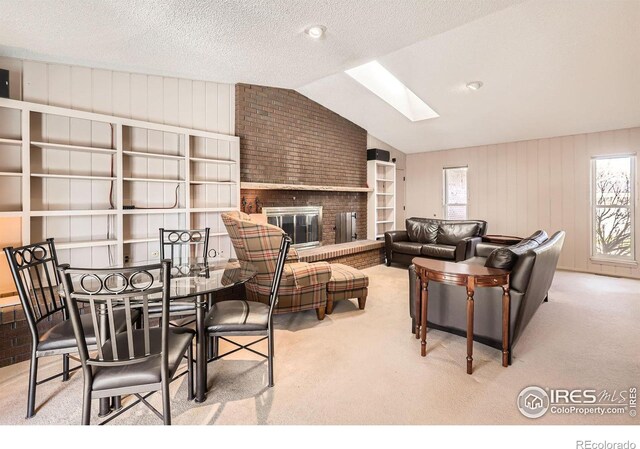 living area with lofted ceiling with skylight, a brick fireplace, carpet floors, and a textured ceiling