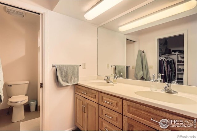 full bathroom featuring double vanity, a spacious closet, toilet, and a sink