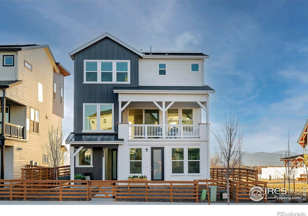 view of front facade featuring a standing seam roof, a fenced front yard, roof mounted solar panels, board and batten siding, and a balcony