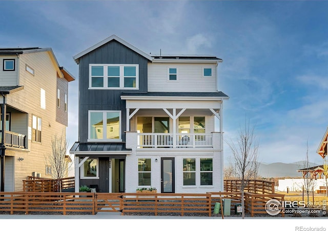 view of front facade featuring a standing seam roof, a fenced front yard, roof mounted solar panels, board and batten siding, and a balcony