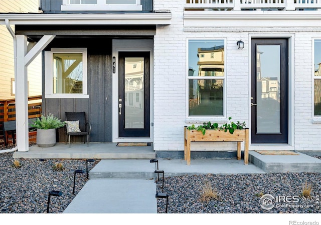 entrance to property featuring brick siding, a porch, and a balcony