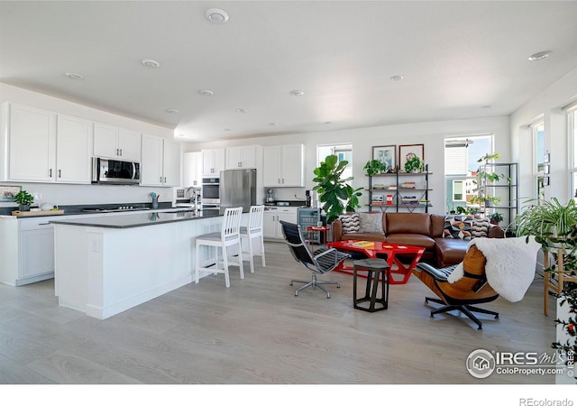 kitchen with light wood finished floors, stainless steel microwave, white cabinets, and a kitchen bar