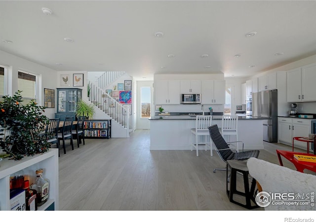 kitchen with dark countertops, a healthy amount of sunlight, light wood-type flooring, stainless steel appliances, and white cabinetry