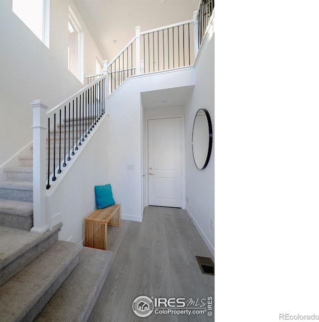 stairway with visible vents, baseboards, a towering ceiling, and wood finished floors