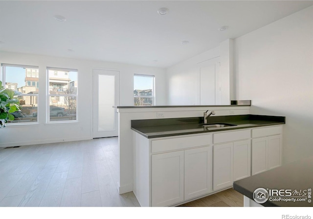 kitchen with a sink, light wood-type flooring, dark countertops, and white cabinetry