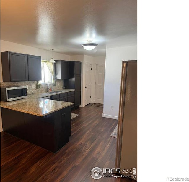 kitchen featuring stainless steel microwave, light stone countertops, a peninsula, dark wood-style floors, and a sink