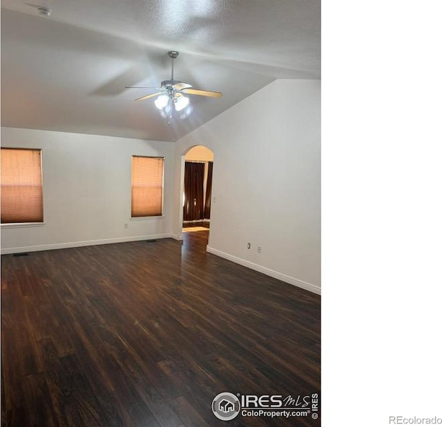 empty room featuring baseboards, lofted ceiling, arched walkways, a ceiling fan, and dark wood-style flooring