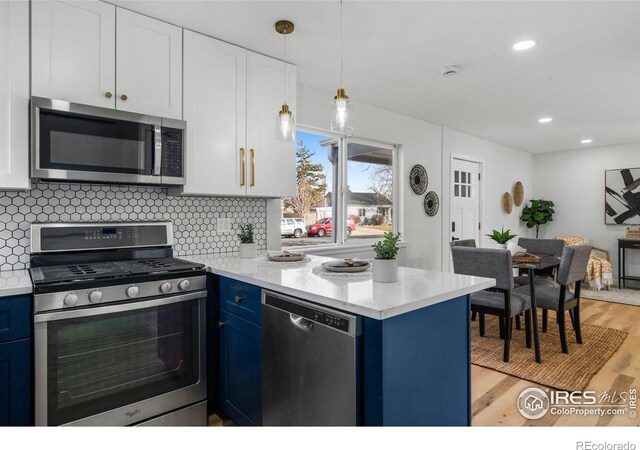 kitchen with a peninsula, blue cabinetry, light wood-style floors, appliances with stainless steel finishes, and backsplash