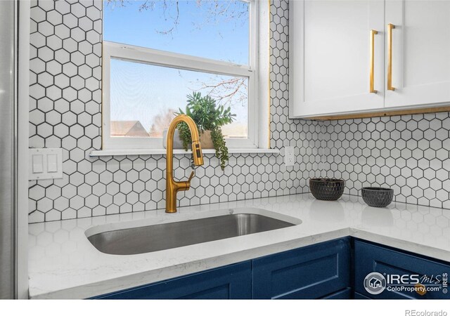 kitchen featuring white cabinets, blue cabinetry, backsplash, and a sink