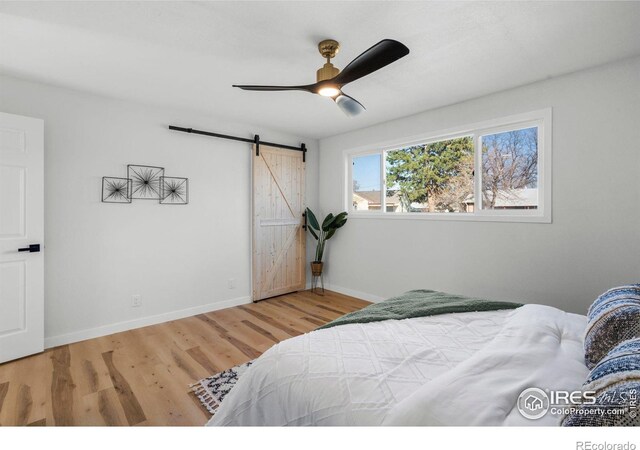 bedroom featuring light wood-type flooring, a barn door, baseboards, and ceiling fan