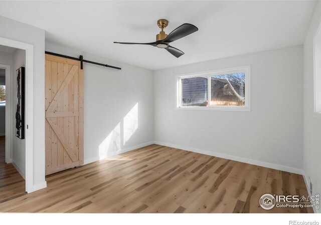 unfurnished bedroom featuring baseboards, light wood-type flooring, a barn door, and a ceiling fan