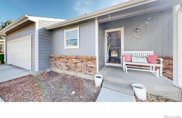 view of exterior entry with a garage, brick siding, covered porch, and concrete driveway