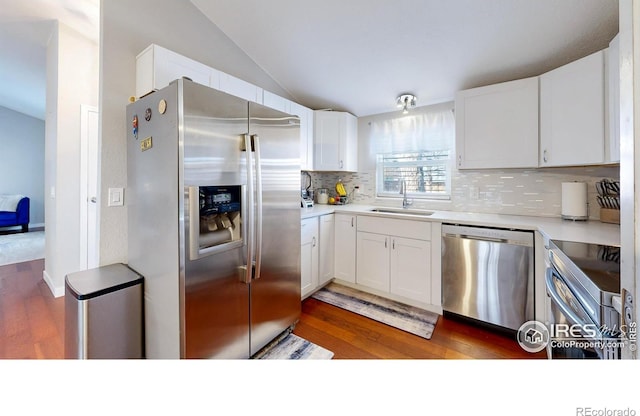 kitchen featuring tasteful backsplash, lofted ceiling, appliances with stainless steel finishes, white cabinets, and a sink