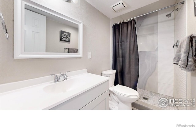 bathroom with visible vents, toilet, a tile shower, vanity, and a textured wall