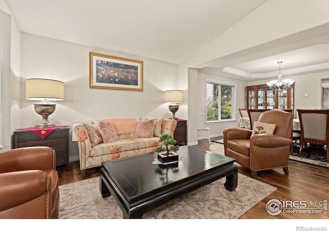 living room with vaulted ceiling, a notable chandelier, a tray ceiling, and wood finished floors