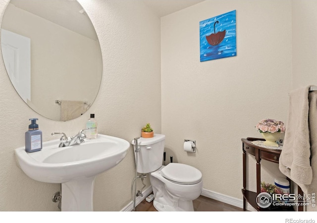 half bathroom with baseboards, toilet, and a textured wall